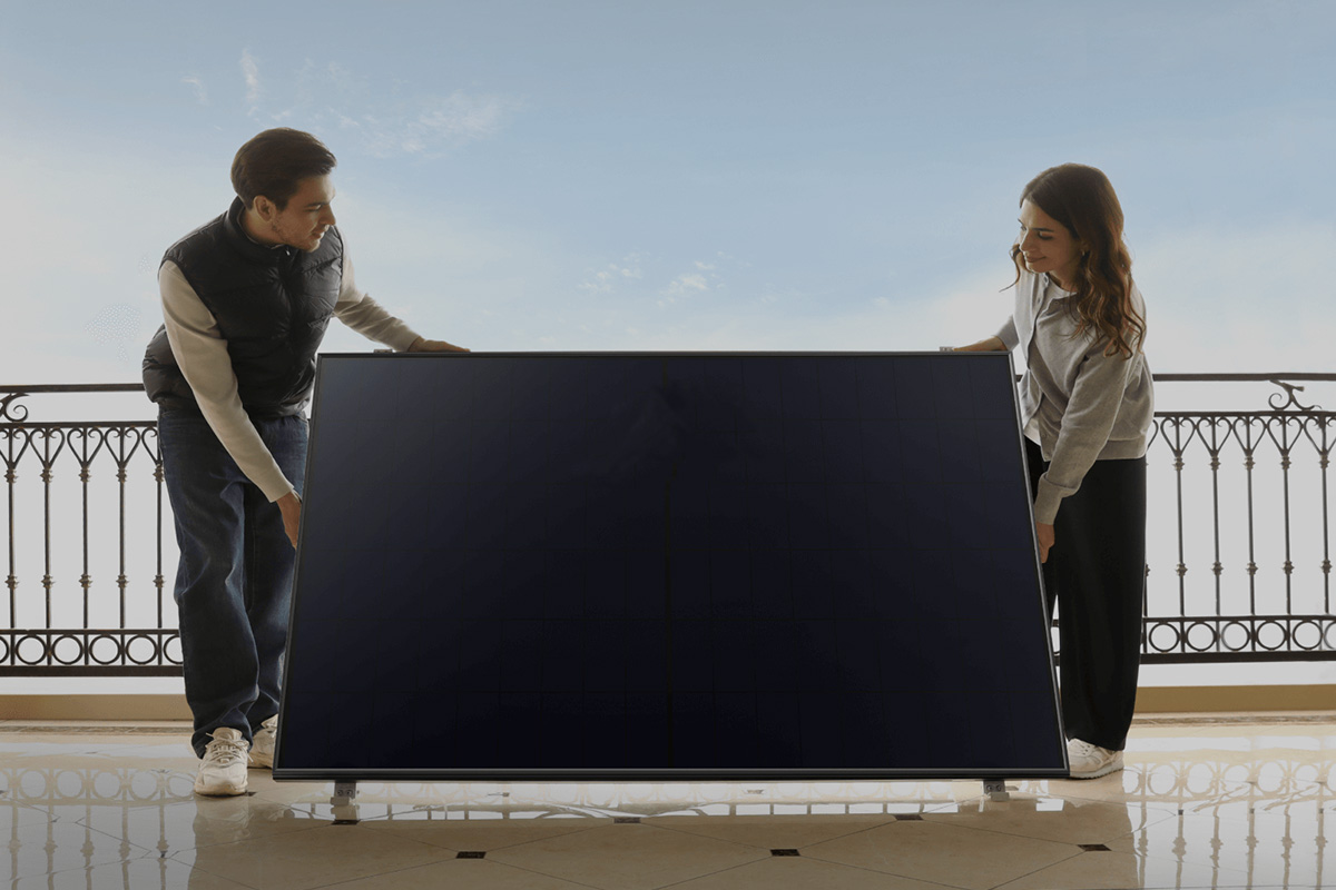 Zwei Personen stehen mit einem Solarpanel auf einem Balkon.