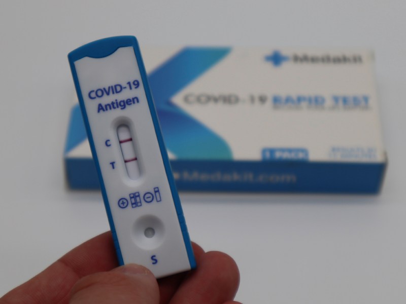 Ein positiver Coronatest wird in der Hand gehalten.