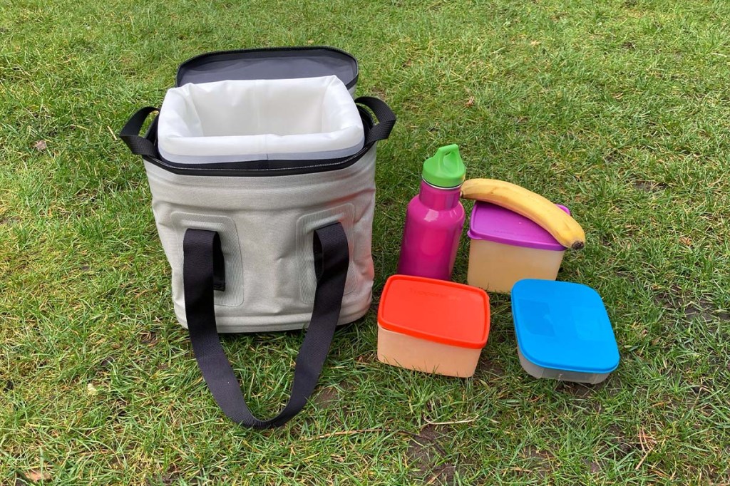 Tasche Go Soft Storage auf dem Rasen stehend, daneben drei Döschen, eine Banane und eine Trinkflasche