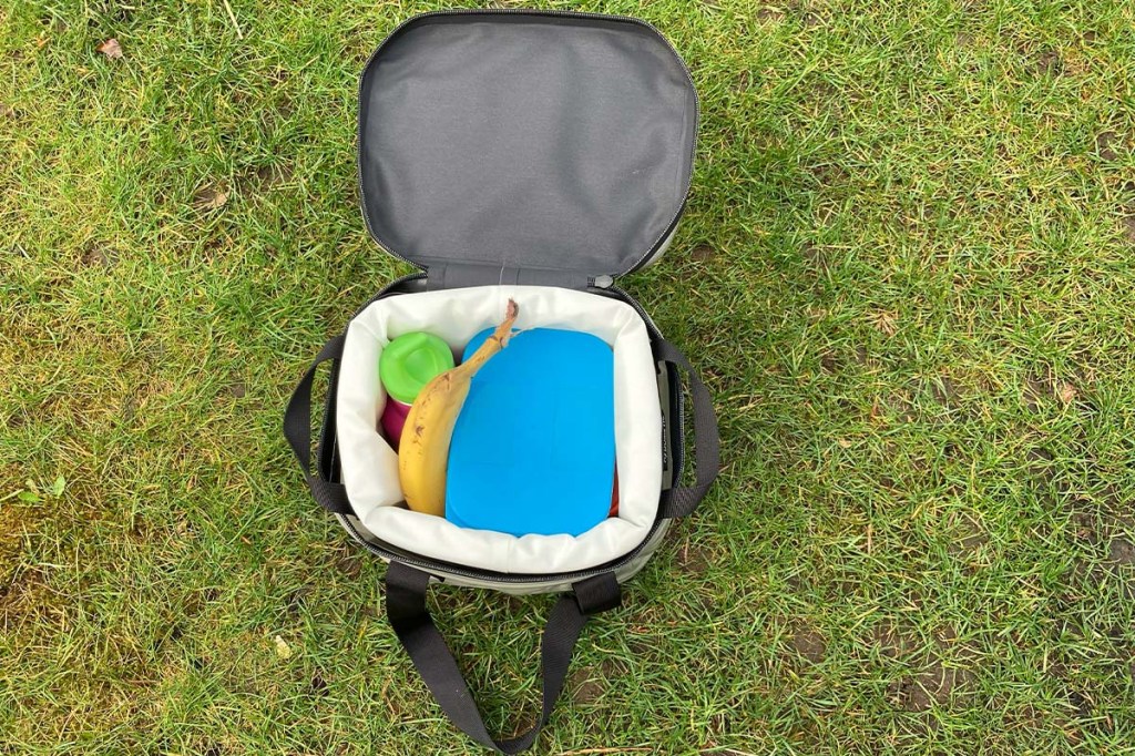 Tasche Go Soft Storage auf dem Rasen stehend, in ihr: drei Döschen, eine Banane und eine Trinkflasche