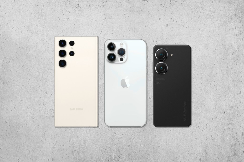 Drei Smartphones in hell und schwarz nebeneinander in unterschiedlichen Größen mit Rückseite nach oben auf marmoriertem Untergrund