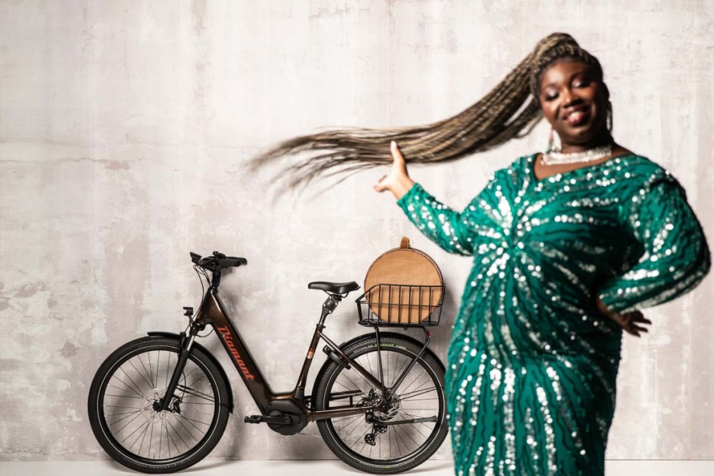 Eine Frau mit grünem Kleid steht in einer Halle, hinter ihr das E-Bike Mandara von Diamant.