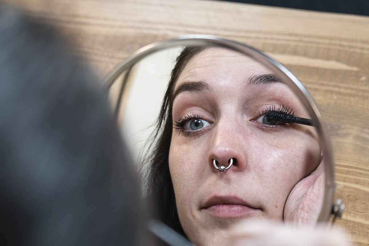 Frau in rundem Kosmetikspiegel trägt Mascara auf