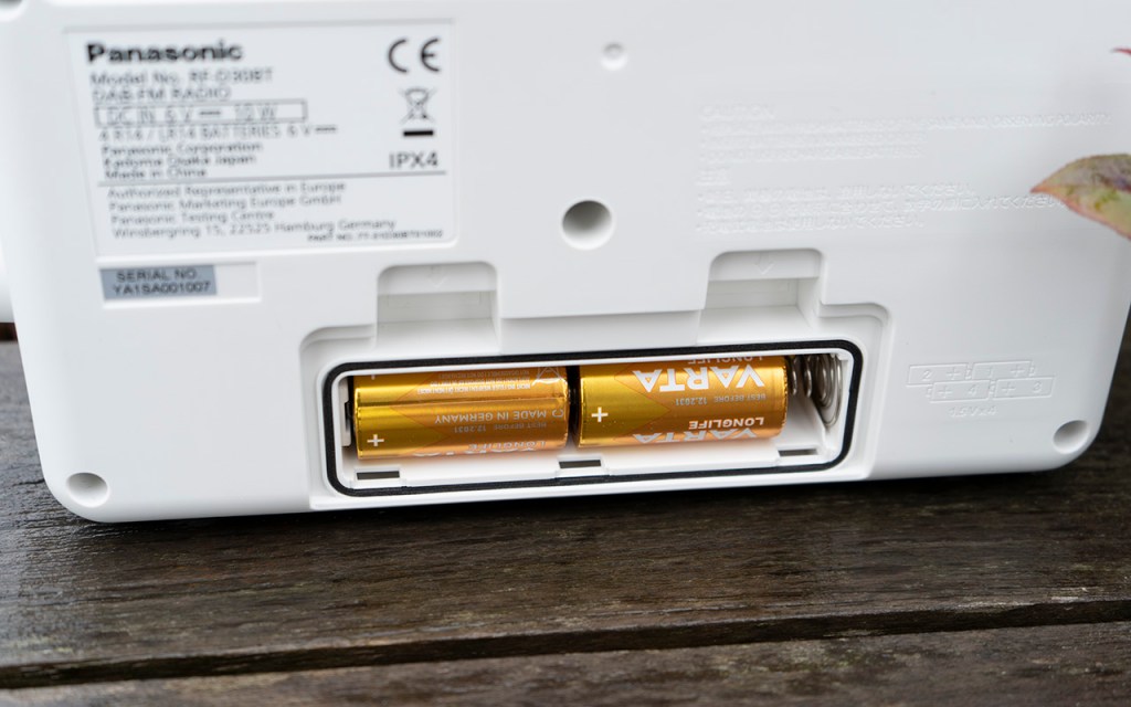 Detail Rückseite weißes Gerät mit geöffnetem Batteriefach in dem zwei goldene Batterien sind.