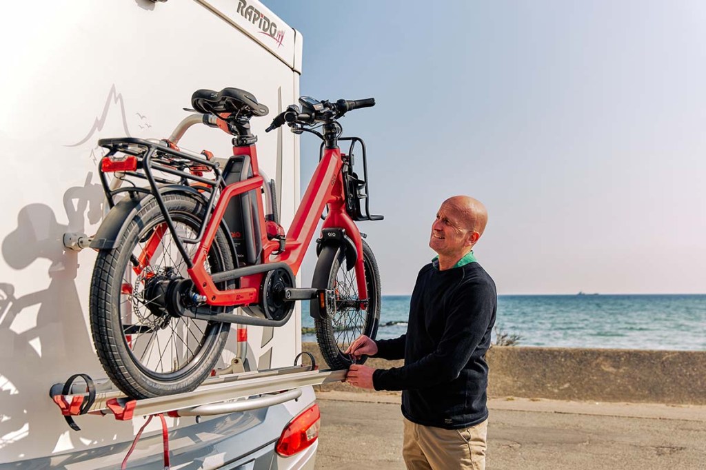 Mann befestigt Kompakt-E-Bike am Heck seines Wohnmobils