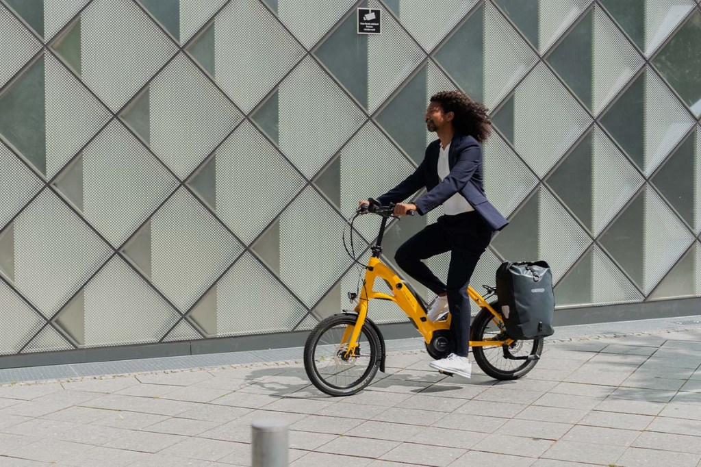 Mann fährt auf Kompakt-E-Bike von Velo de Ville an einer Häuserfront entlang