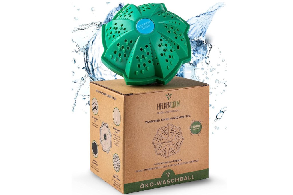 Eckiger Karton schräg von vorne mit grünem geschwungenem Plastikball mit Löchern umgeben von Wasserspritzern auf weißem Hintergrund