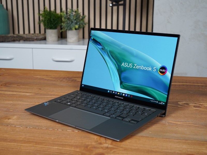 Das Asus Zenbook 13 OLED steht schräg auf einem Holztisch.