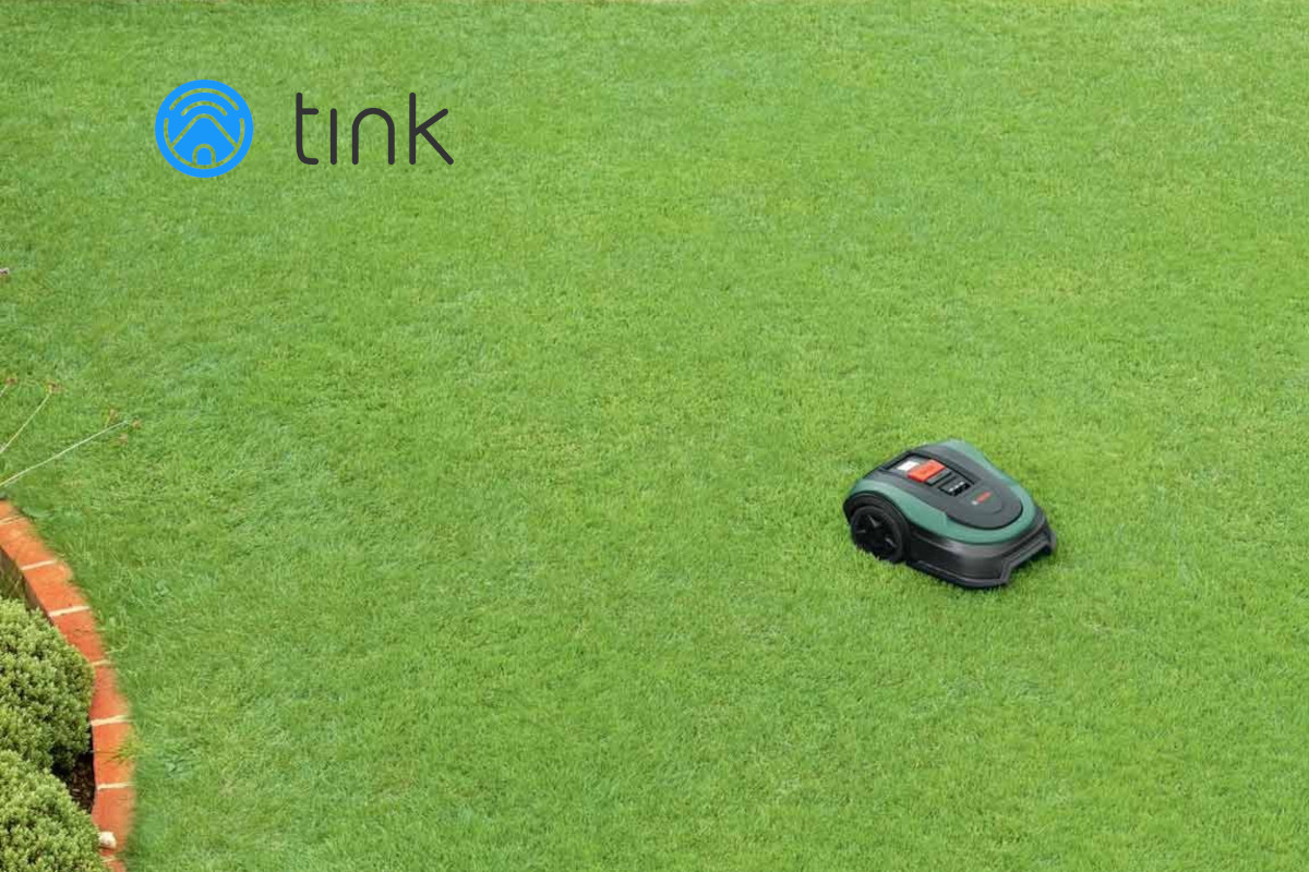Grüne Rasenfläche von oben mit dunkelgrünem Bosch Mähroboter rechts mittig und Tink-Logo links oben