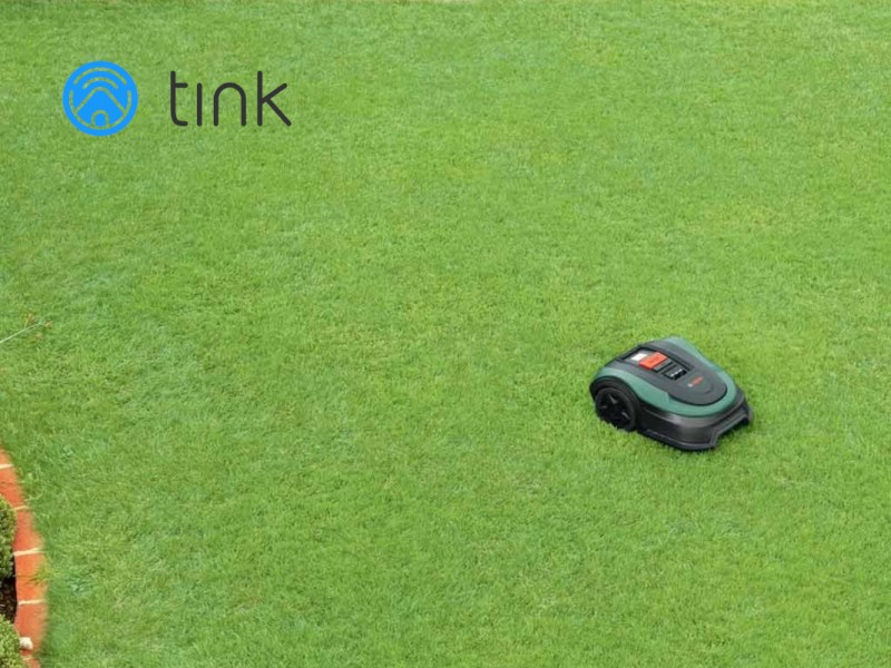 Grüne Rasenfläche von oben mit dunkelgrünem Bosch Mähroboter rechts mittig und Tink-Logo links oben