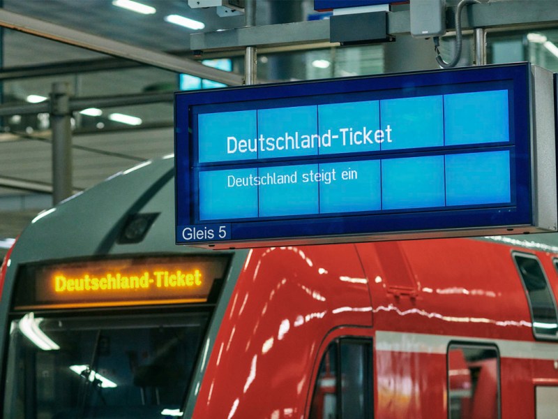 Informationsanzeige an einem Bahnsteig mit Regionalzug im Hintergrund.