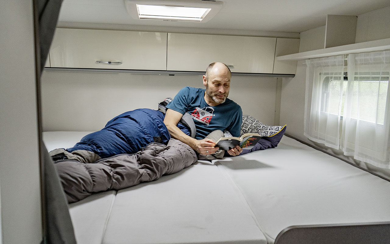 Mann liegt im Schlafbereich des teilintegrierten Wohnmobils Etrusco T 7.3 SF.