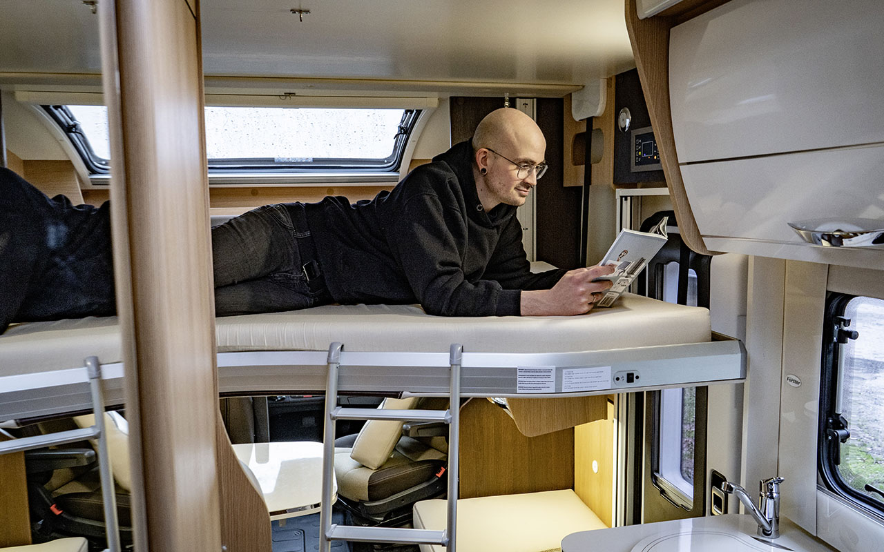 Mann liegt in einem Hubbett in einem Wohnmobil und schaut aufs Smartphone.