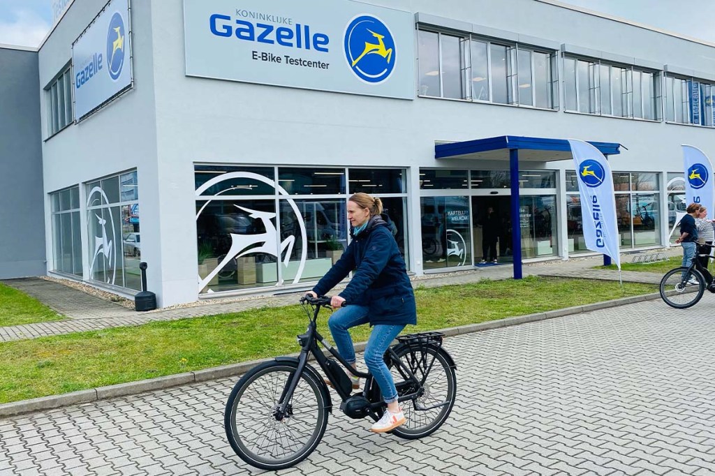 Frau fährt auf E-bike, Gazelle-Testcenter im Hintergrund