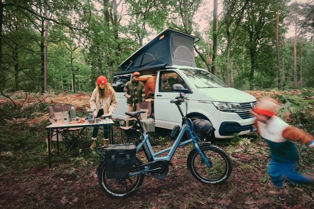 Familie mit ihrem Campervan im Wald, im Vordergrund ein kompaktes E-Bike von Kalkhoff