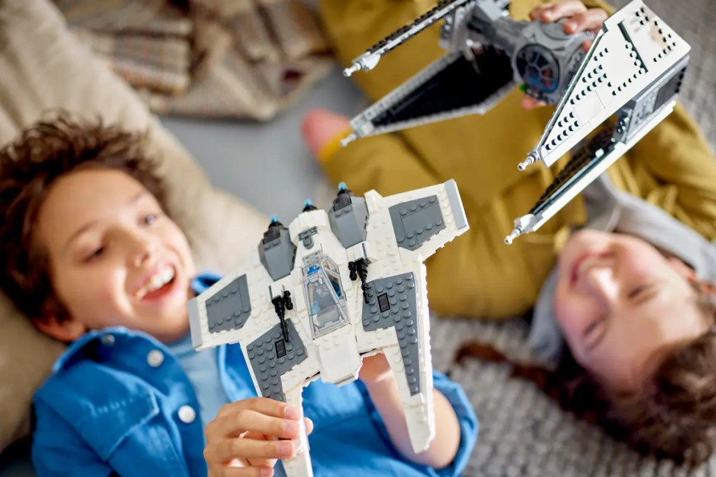Zwei Kinder halten je ein Raumschiff aus lego hoch auf den Rücken liegend