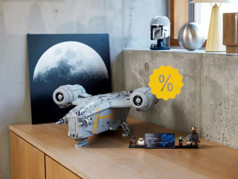 Graues Lego Star Wars Raumschiff aufgebaut auf Holztisch vor Steinwand und Mondbild mit gelben Prozentzeichen rechts mittig