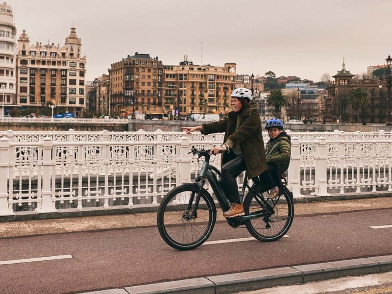 Frau fährt mit Kiind im Kindersitz dem fahrrad durch eine Stadt.