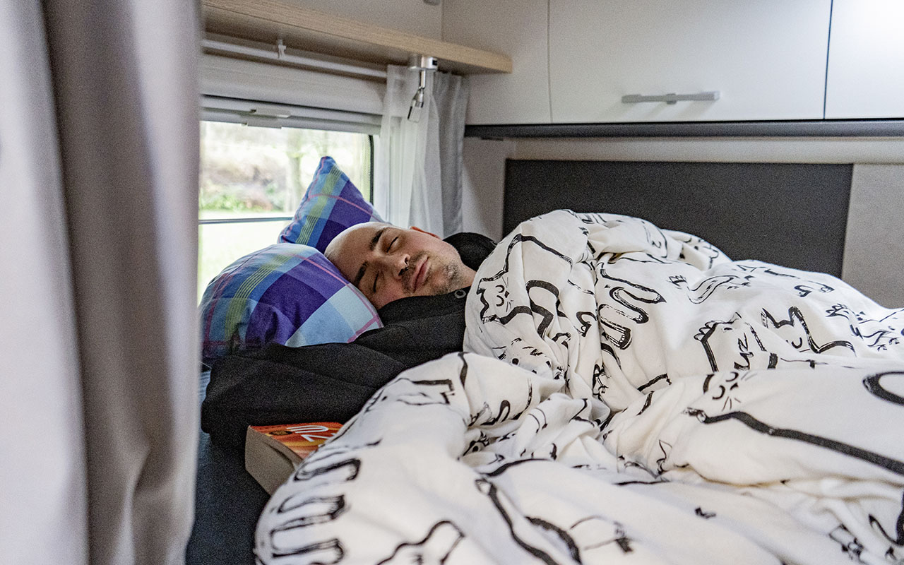 Mann liegt im Bett. Detailbild Innenansicht Schlafbereich im Wohnmobil Sunlight A70 Adventure Line.