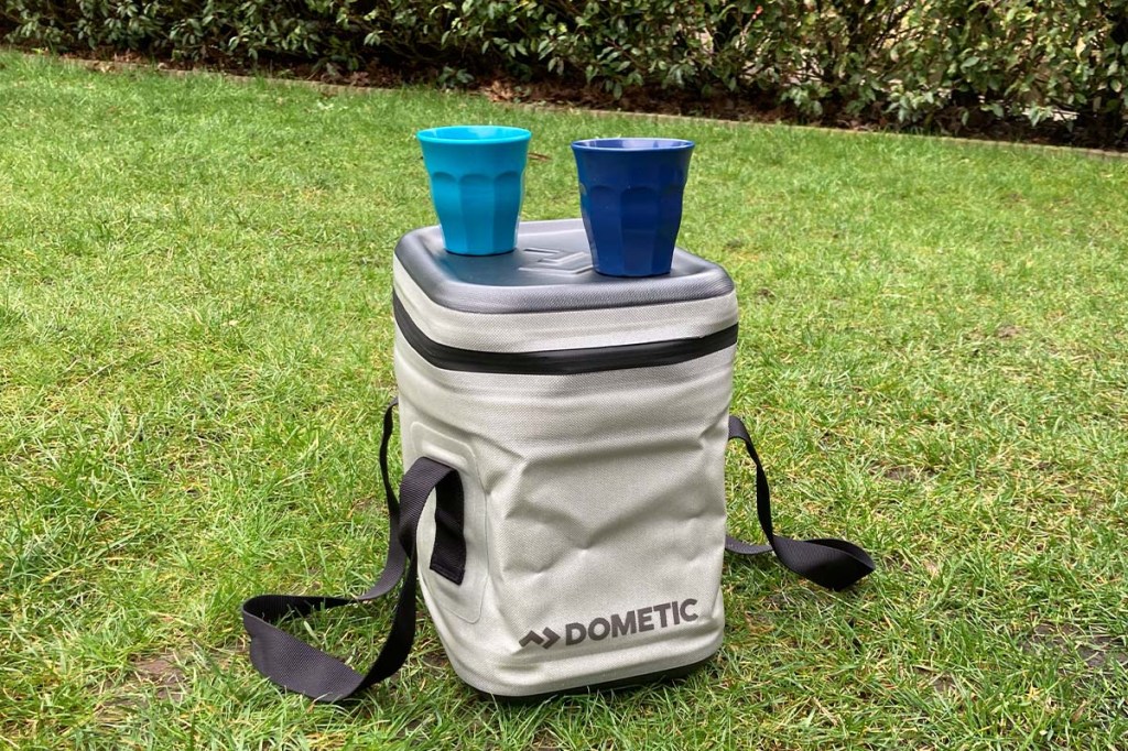 Kühltasche Dometic Go Soft Storage auf einer Wiese, auf dem Deckel stehen zwei Becher