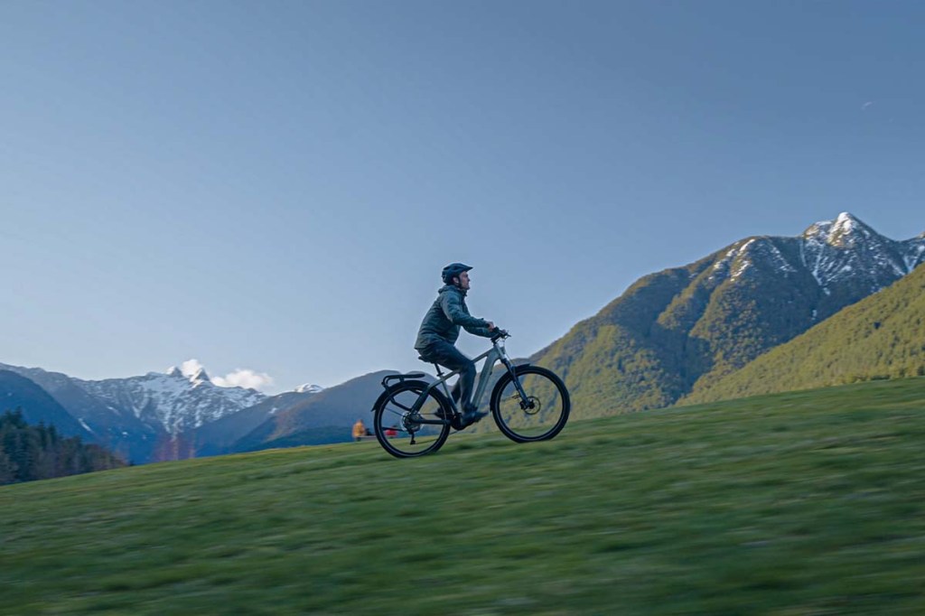 Mann fährt mit E-bike von Tenways einen Berg hoch, Berglandschaft im Hintergrund