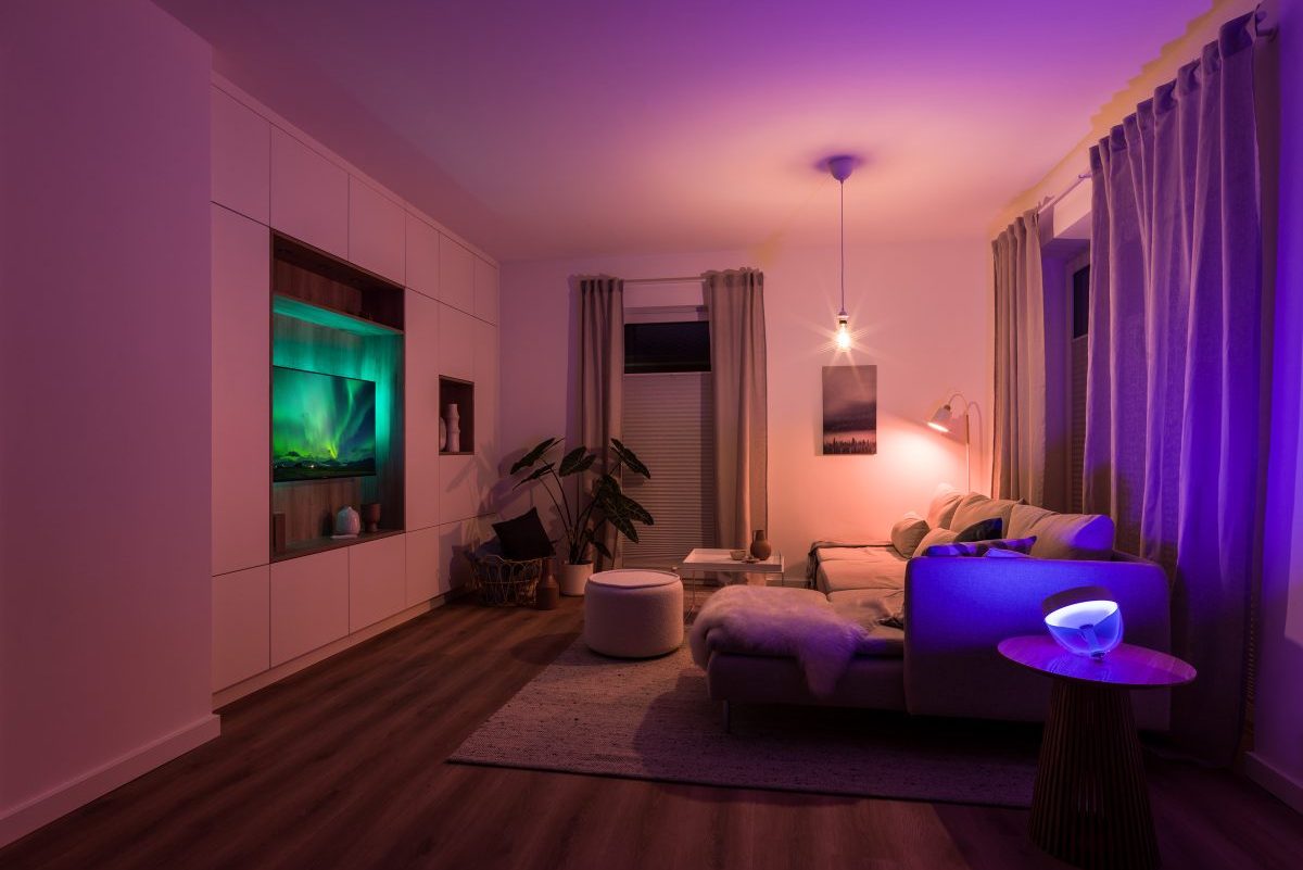 Ein gemütliches Wohnzimmer mit Fernseher, das lila-orange durch smarte Lampen beleuchtet ist.