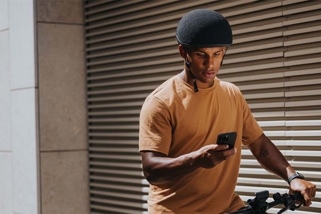 Mann steht neben seinem Fahrrad, hat sein Smartphone in der Hand und schaut darauf