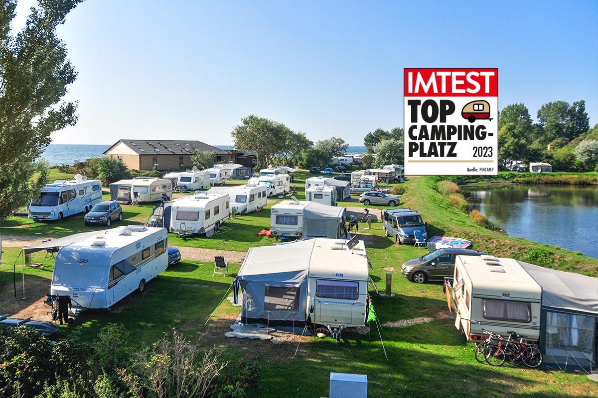 Campingplatz mit grünen Flächen und weißen Wohnwagen von oben mit blauem Himmel und IMTEST-Siegel Top Campingplatz