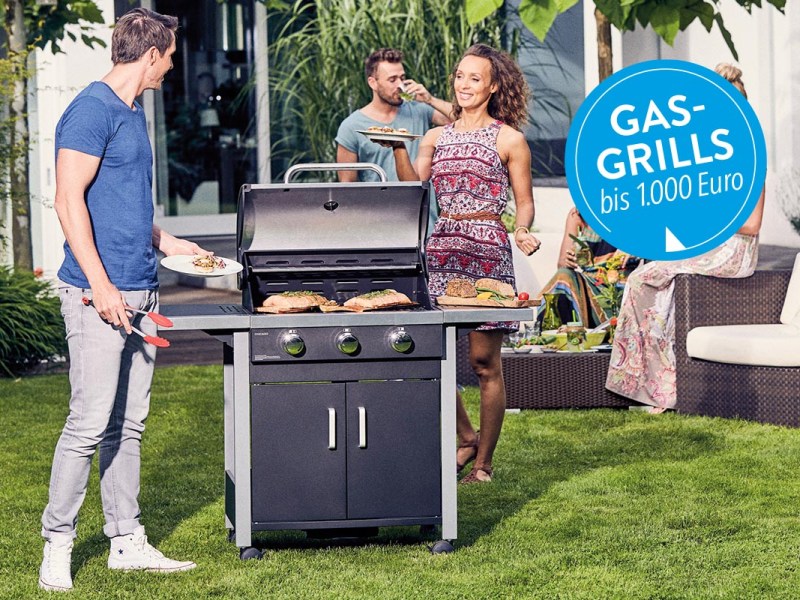 Ein Gasgrill in einem Garten auf Rasen neben Personen stehend.