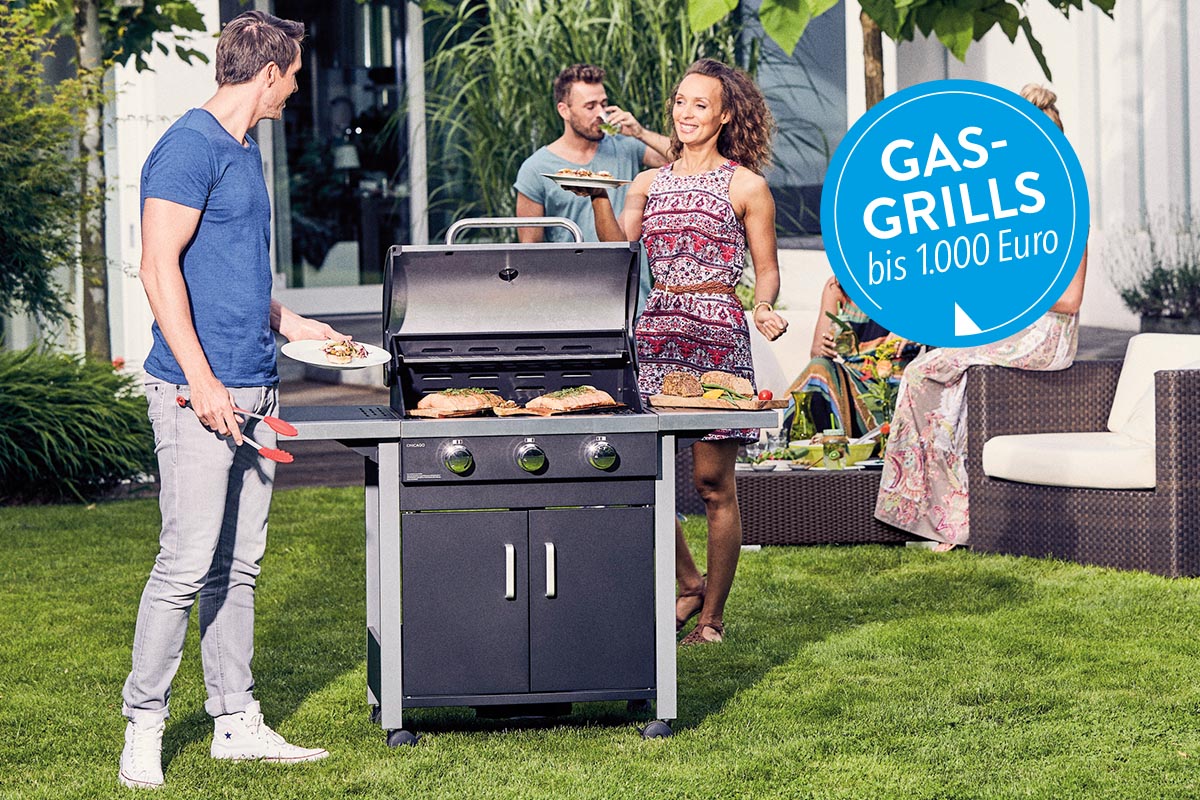 Ein Gasgrill in einem Garten auf Rasen neben Personen stehend.