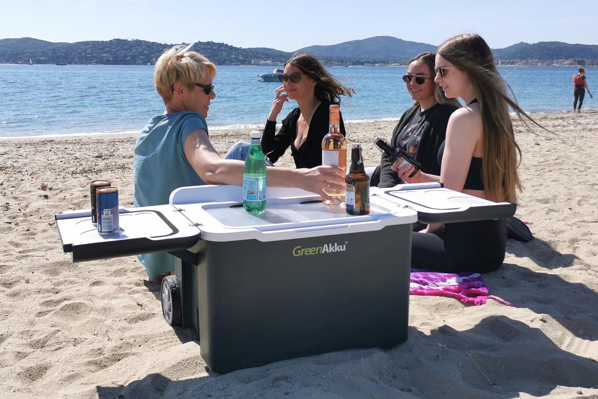 Vier Frauen an einem Strand sitzend mit einer Kühlbox von GreenAkku.