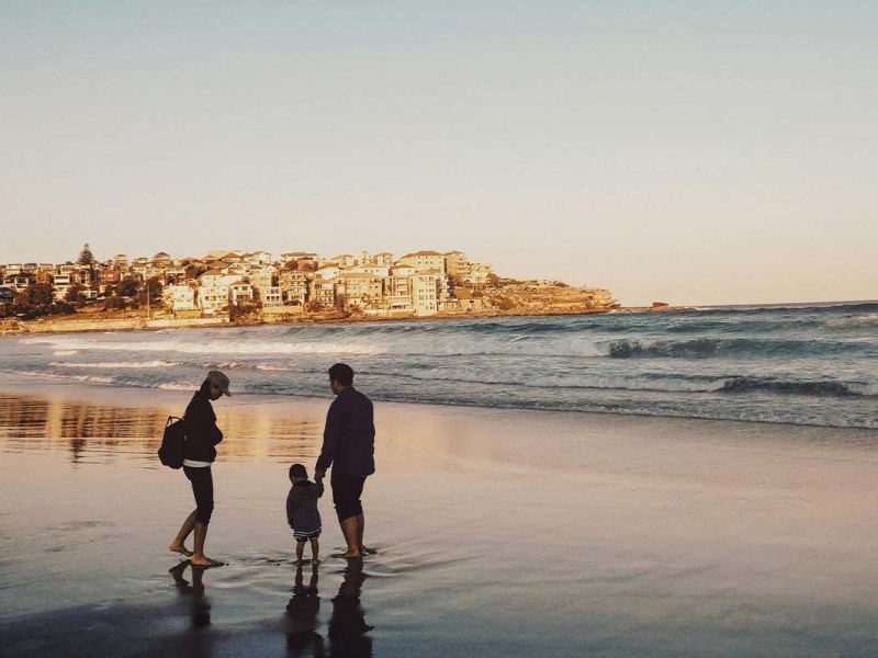 familie bei sonnenuntergang an einem Strand, im Hintergrund sieht man einen Küstenort