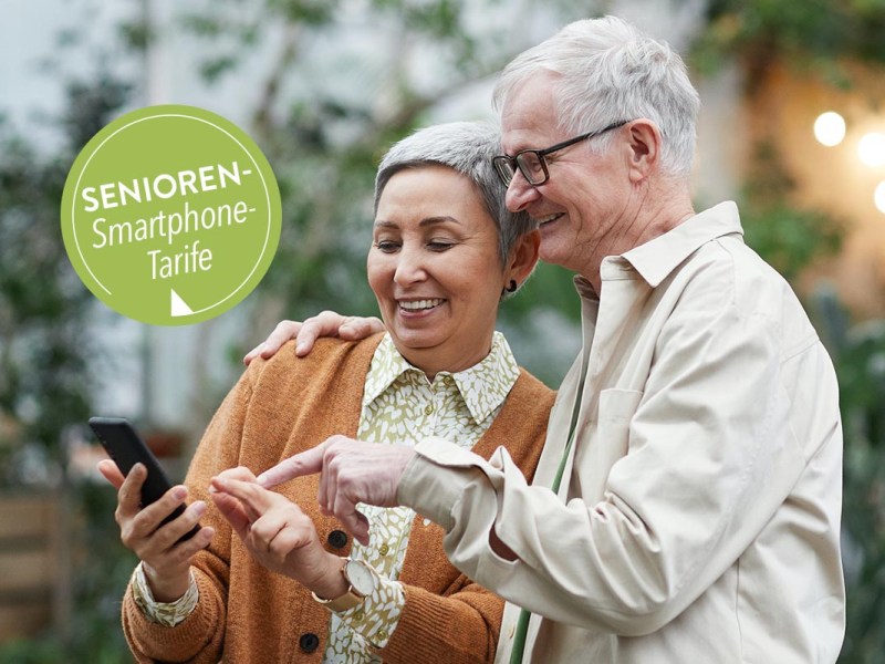 Zwei ältere Personen unter freiem Himmel mit einem Handy in der Hand.