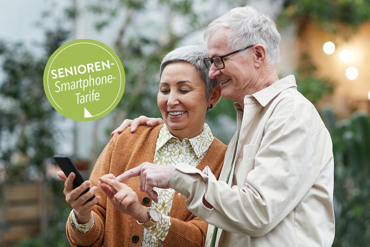 Zwei ältere Personen unter freiem Himmel mit einem Handy in der Hand.