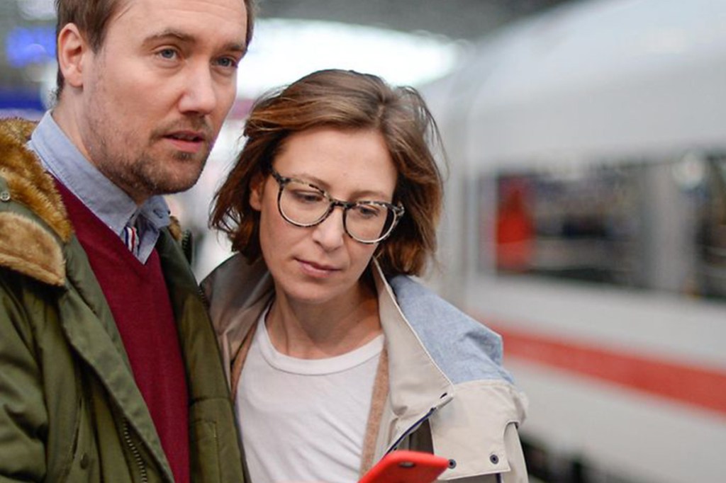 Zwei Menschen stehen vor einem Zug und schauen auf ein Handy.
