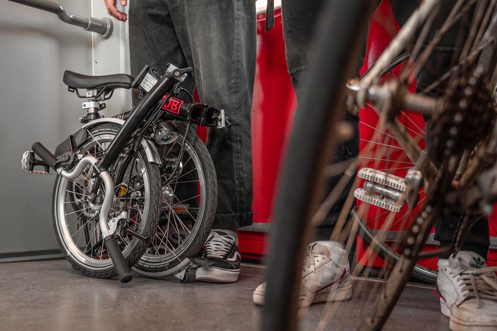 Man steht in einem Bahnabteil der Deutsche Bahn mit einem zusammengefalteten Fahrrad zwischen den Beinen.