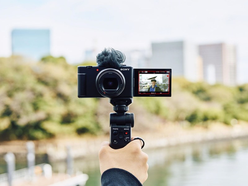 Sony ZV-1 II auf einem Hand-Gimbal montiert für eine Selfie-Aufnahme vor einem Stadtpark.
