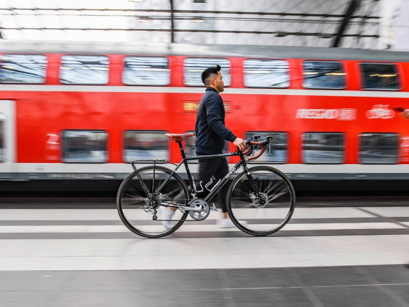 Ein Mann läuft mit einem Fahrrad am Bahnsteig entlang.