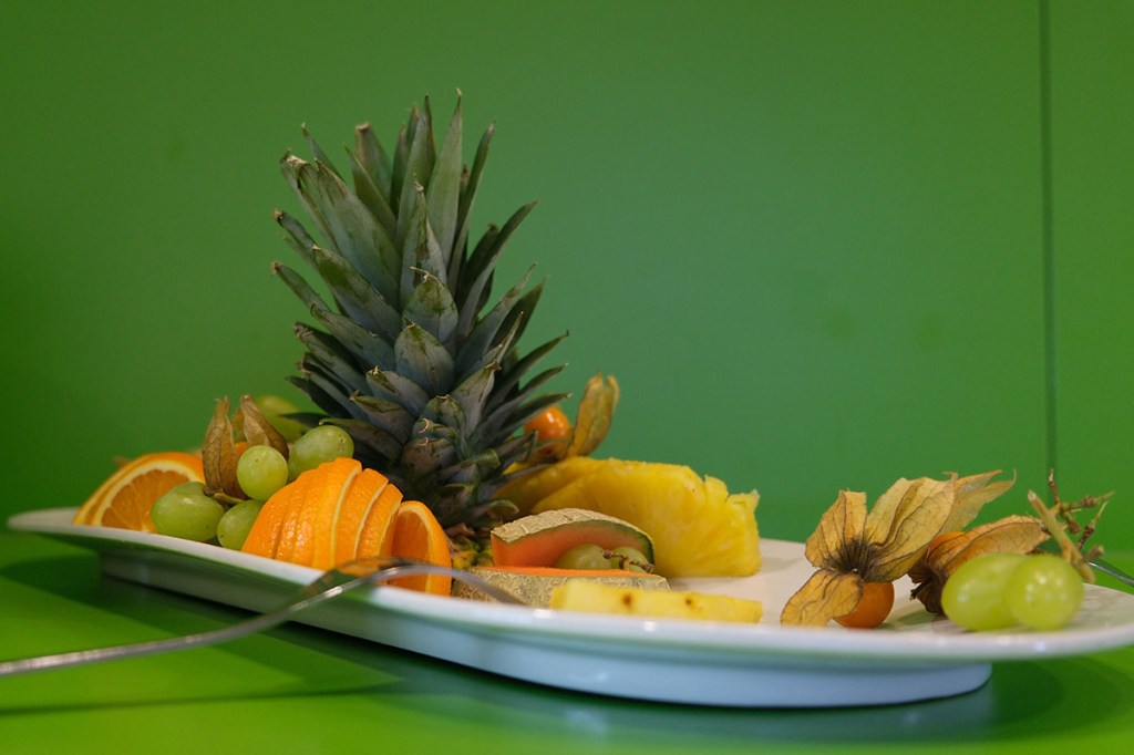 Obstteller mit Ananas und Orangen vor grüner Wand