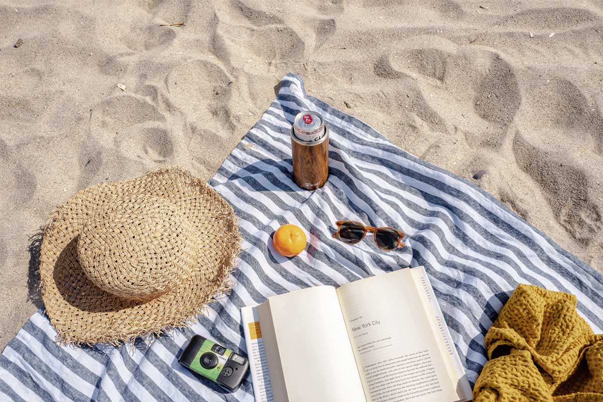 Eine Strandmatte mit Sonnenbrille, Hut, Kamera und offenem Buch.