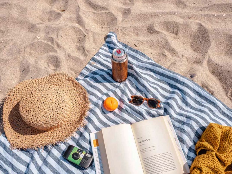 Eine Strandmatte mit Sonnenbrille, Hut, Kamera und offenem Buch.