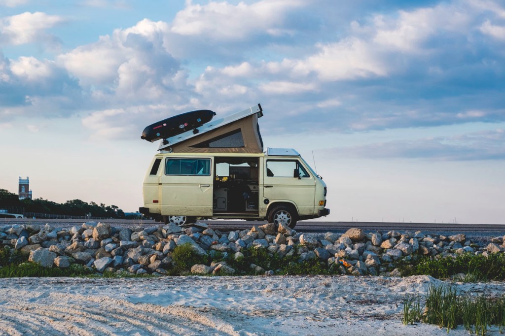 Ein Campervan steht auf einer einsamen Straße vor einem Strand.