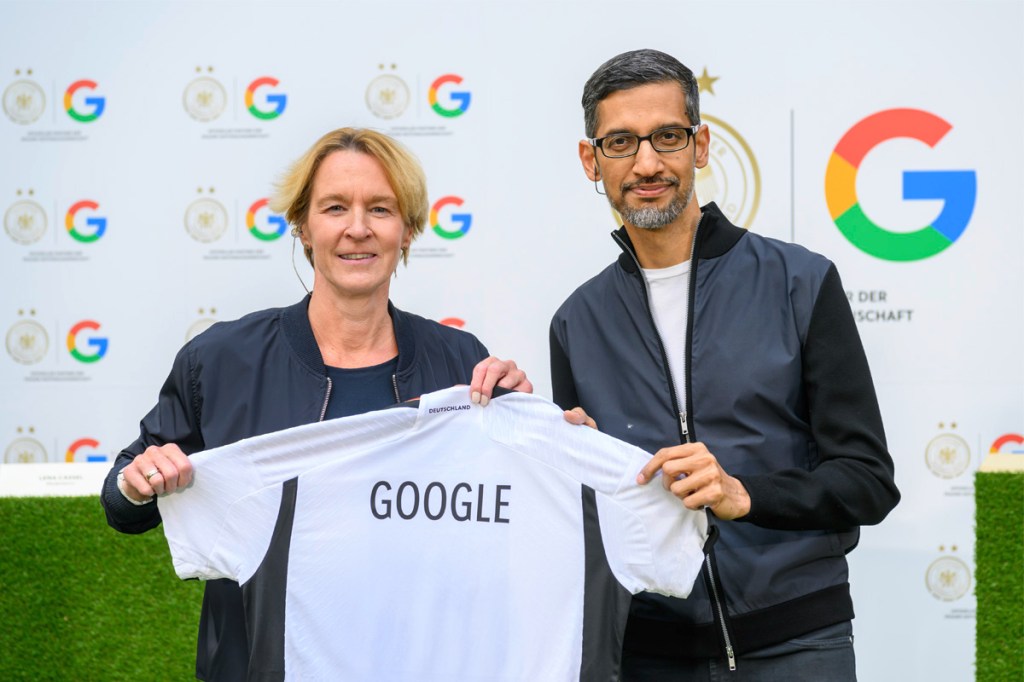 Martina Voss-Tecklenburg und Sundar Pichai halten gemeinsam ein Trikot, auf dem Google steht. 