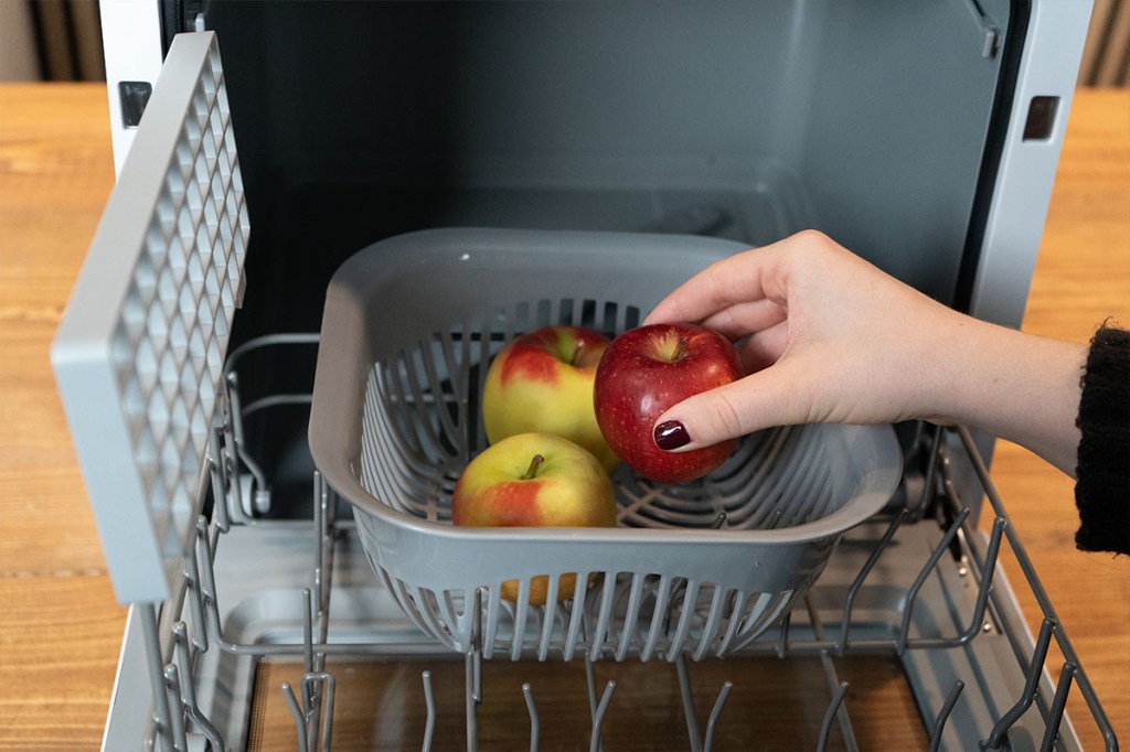 Ein Apfel wird in die Obstschale des Tischgeschirrspülers gelegt.