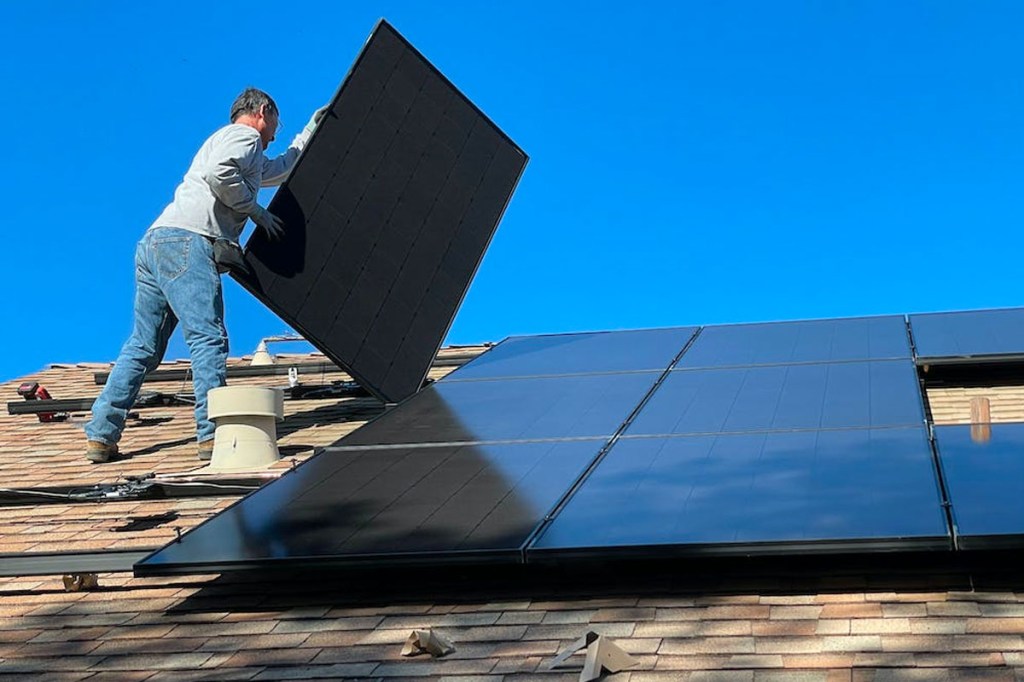 Eine Person installiert ein Solarpanel auf einem Hausdach.