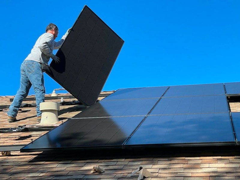 Eine Person installiert ein Solarpanel auf einem Hausdach.