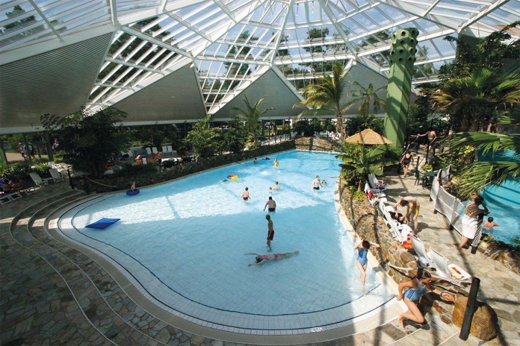 Pool unter Glasdach mit Palmen und Menschen