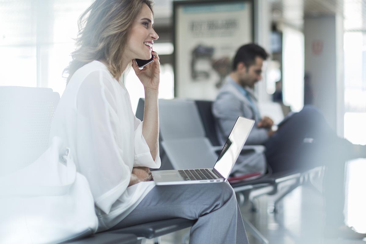 Eine Frau sitzt mit Smartphone und Notebook am Flughafen
