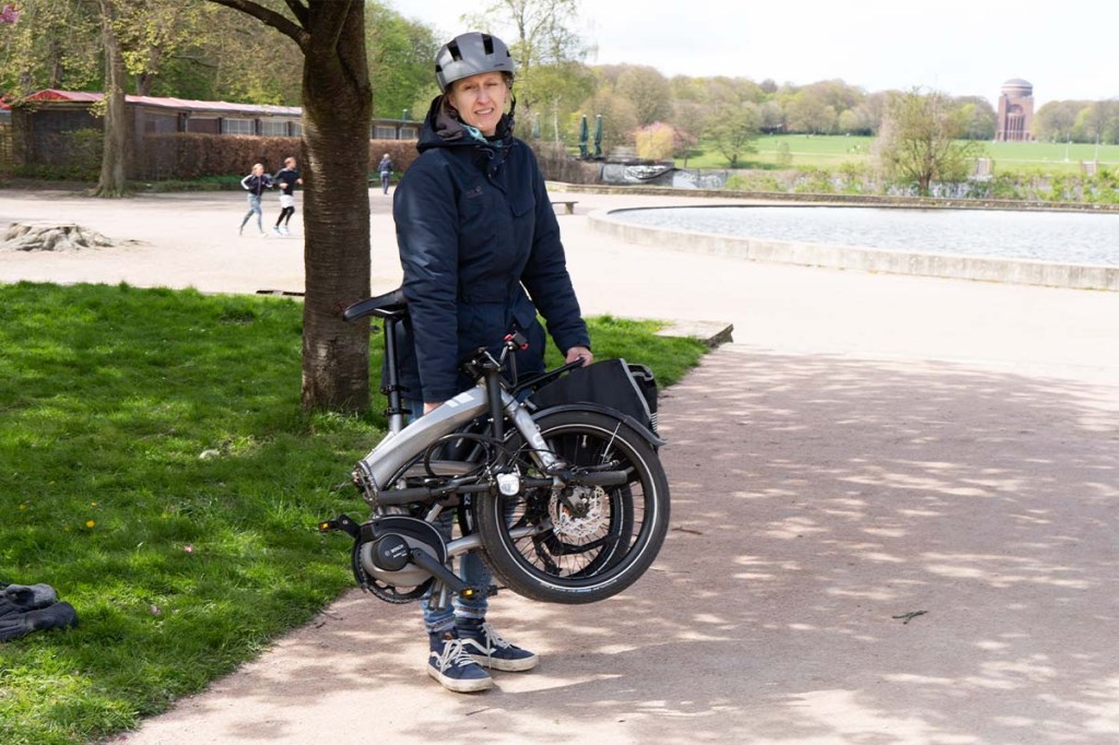 Frau trägt zusammengefaltetes E-Bike im Park