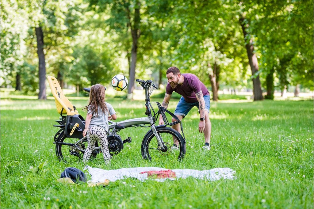 Man spielt auf der Wiese mit seinem Kind, neben ihm sein Falt-E-Bike von Tern